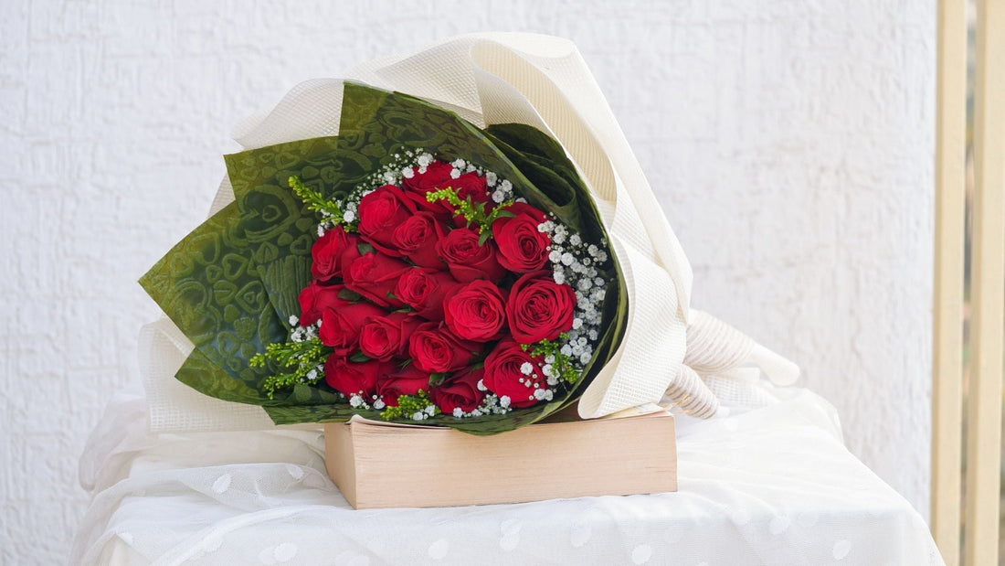 legant bouquet of fresh red roses wrapped in white and green decorative paper, placed on a wooden box with a soft white fabric backdrop, perfect for Valentine's Day or special occasions.