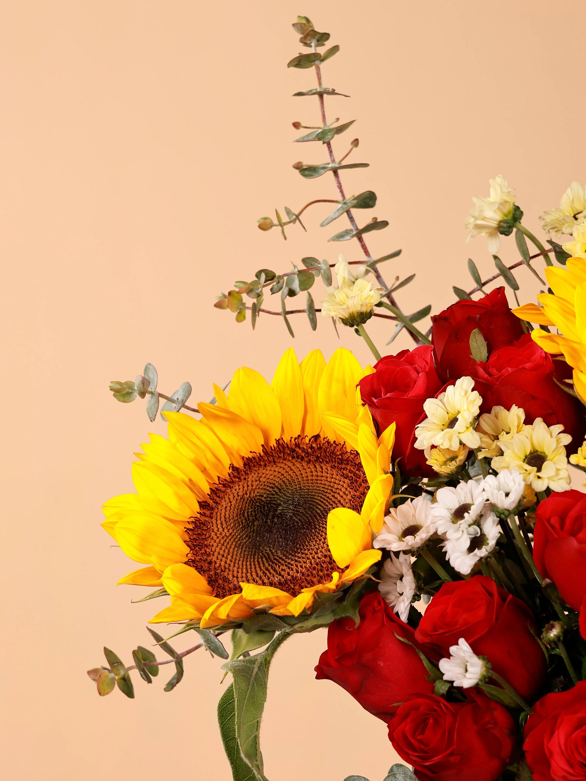 Close-up of a sunflower in a vibrant bouquet with red roses and white daisies