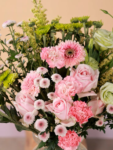 Close-up of a lush and full floral arrangement featuring Sweet Avalanche roses, pink carnations, pink gerberas, green chrysanthemums, green eustoma, and light calimero