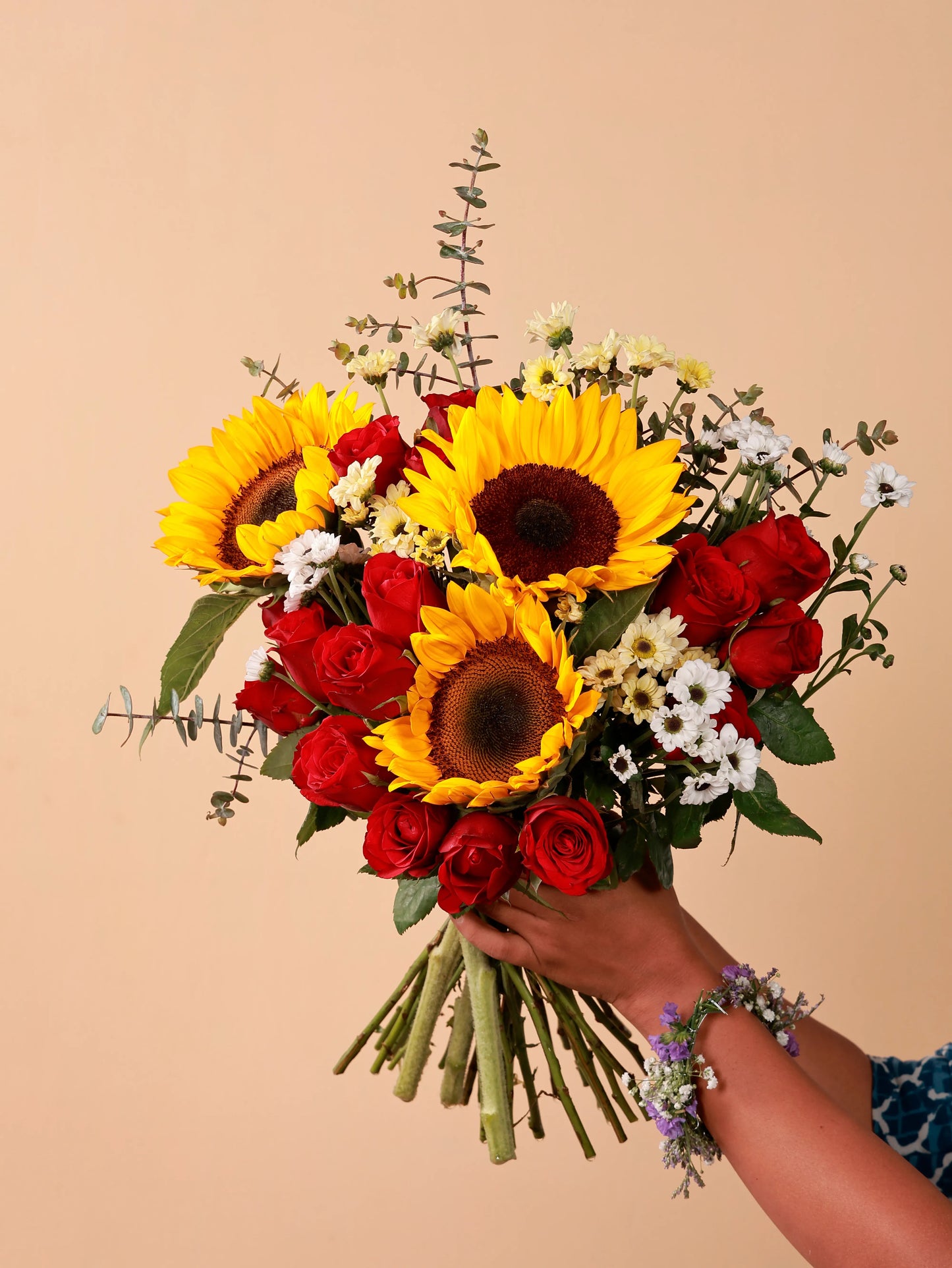 A hand holding a bouquet of sunflowers, red roses, and white daisies