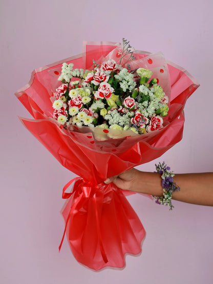 Beautifully wrapped floral bouquet in red cellophane with a ribbon, held by a hand wearing a floral wristlet