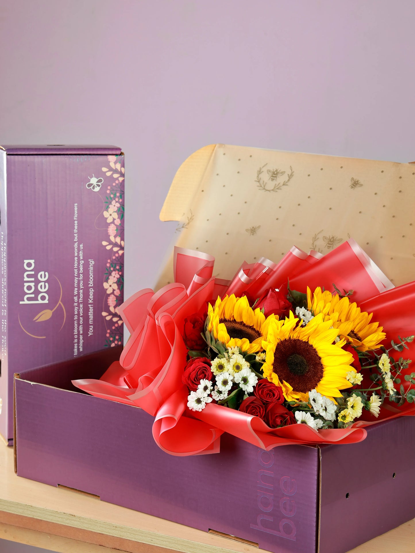 A bouquet of sunflowers and red roses in a gift box with the Hanabee logo